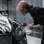 Una ragazza pulisce i fari della propria auto con dei prodotti specifici